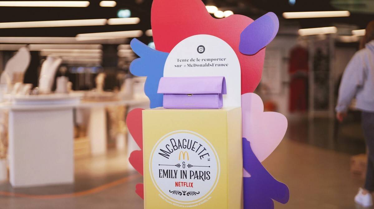 mcbaguette-tbwa A rectangular purple clutch purse sits atop a podium in a department store, with a sign that says
