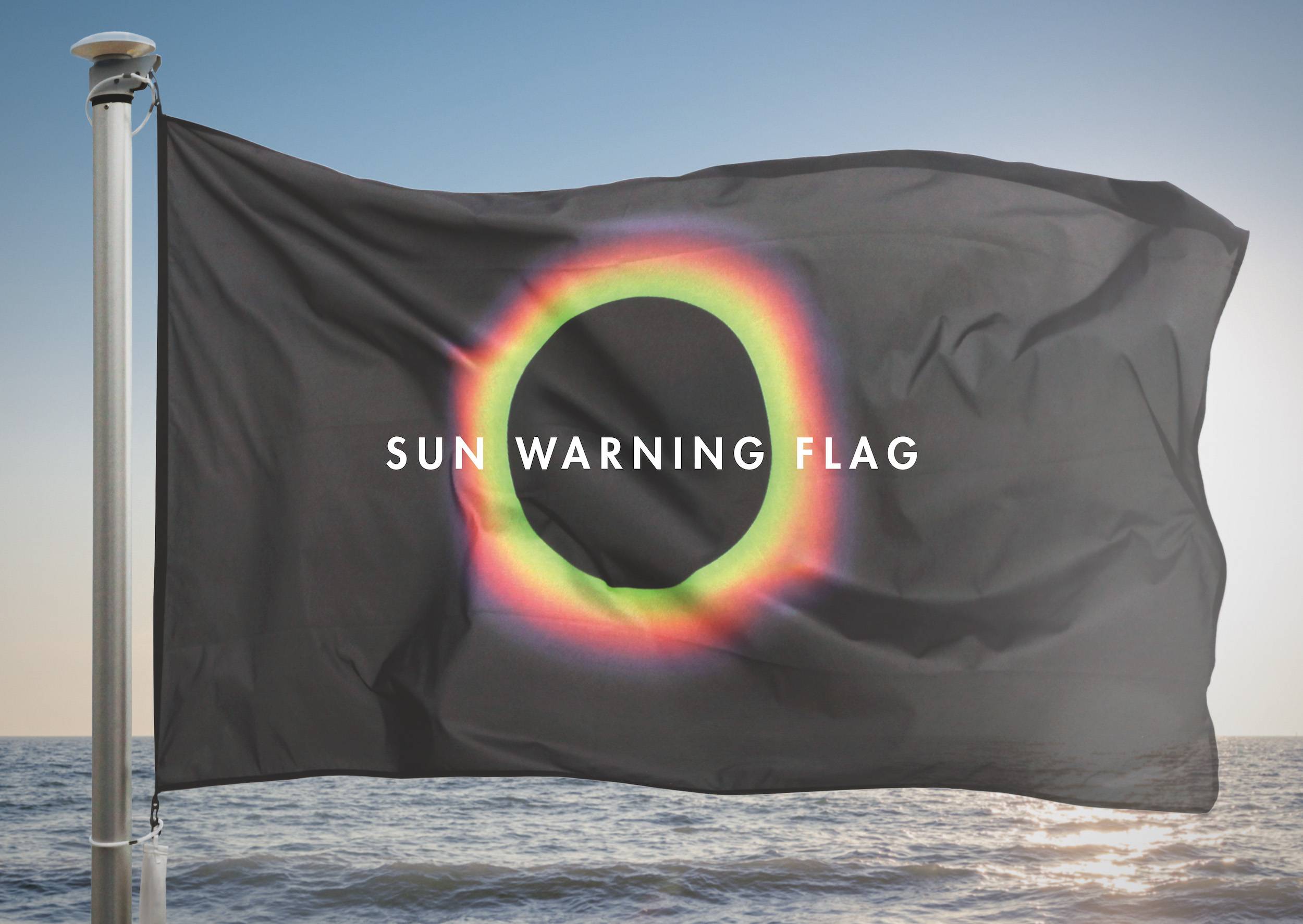 A large black flag with a circle of light that says "Sun Warning Flag", on display at a beach