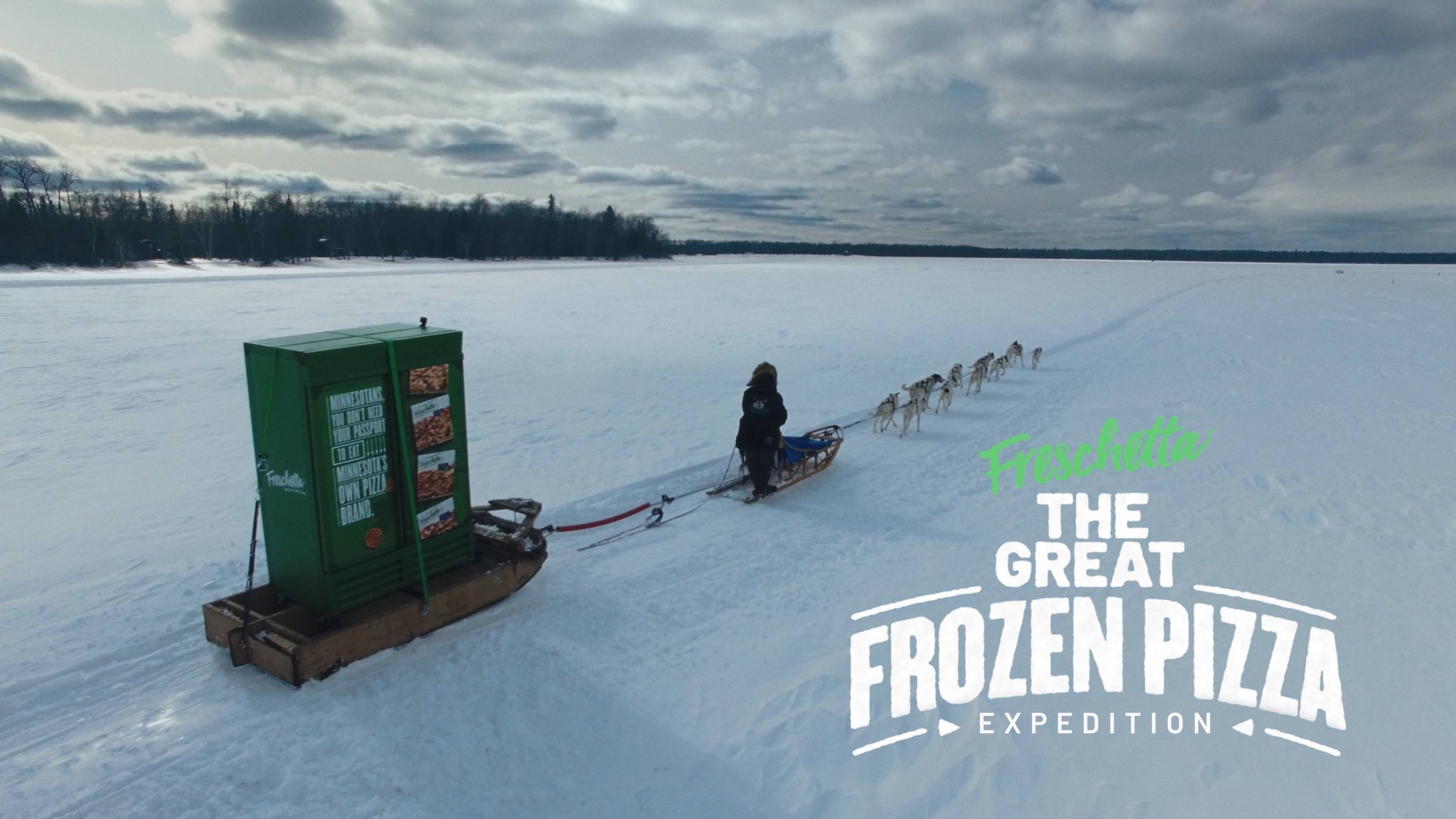 A dog sled pulls a giant freschetta pizza freezer over a frozen lake