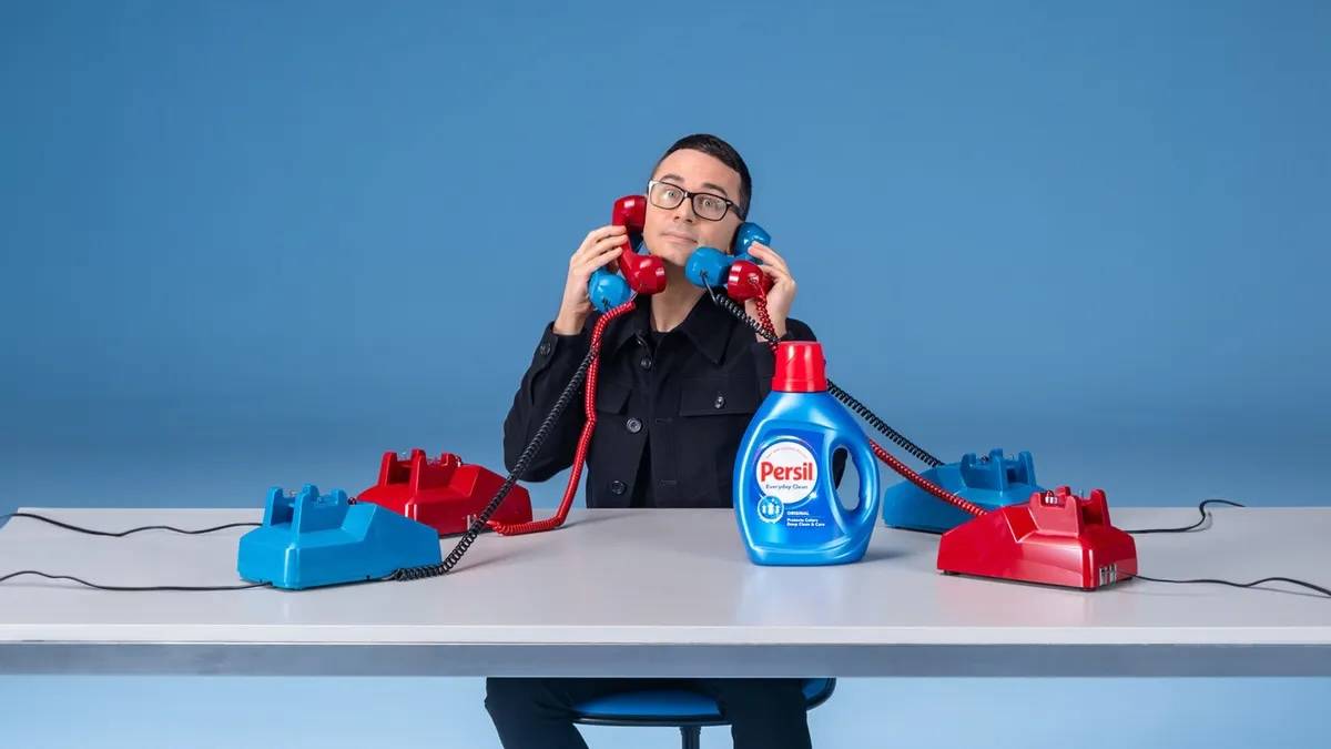 Persil_First_Ever_24_Hour_Wardrobe_Refresh_Hotline_1 fashion designer christian siriano sits at a table answering phones