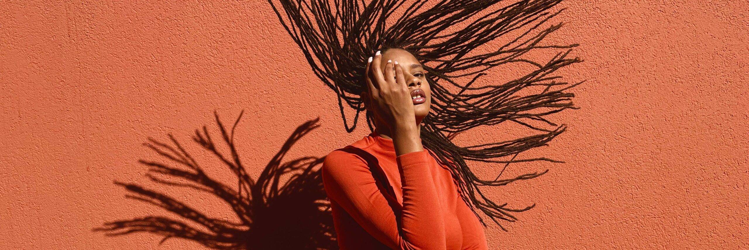 Shot on iPhone “Hometown” campaign-DTLA (1) a woman flips her hair against the backdrop of an orange wall